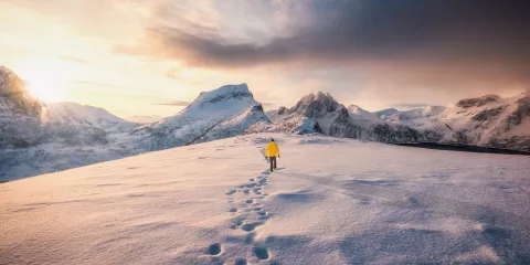 Mountaineer walking with footprint in snow storm and sunrise over snowy mountain in Senja Island